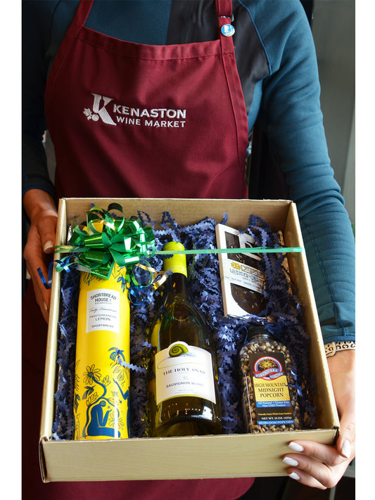 Person wearing a Kenaston Wine Market apron holding a gift box with wine and popcorn kernels.